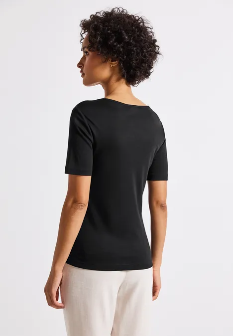 Frau mit lockigem Haar trägt schwarzes T-Shirt und helle Hose, Blick nach hinten.